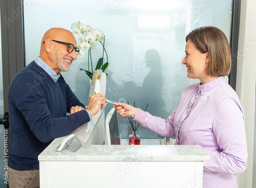 Senior patient giving his health insurance card to the dentist secretary