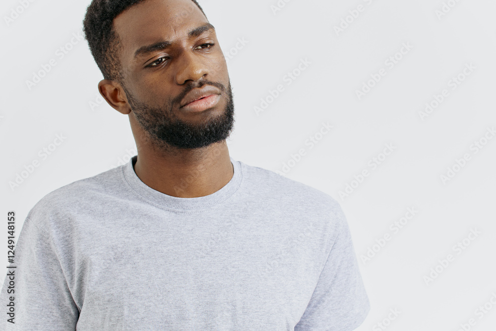 Fototapeta premium Confident young man in casual grey tshirt standing with hands on hips against a plain white background