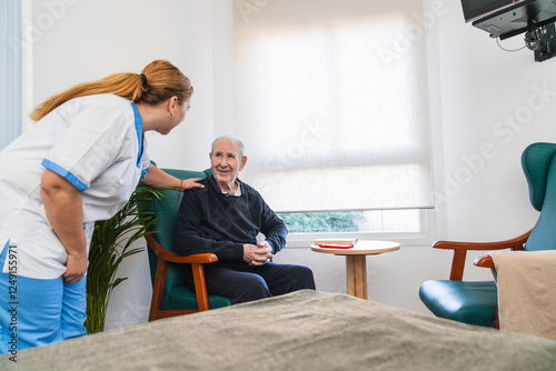 Obraz na plátně Nurse comforting elderly man sitting in nursing home room