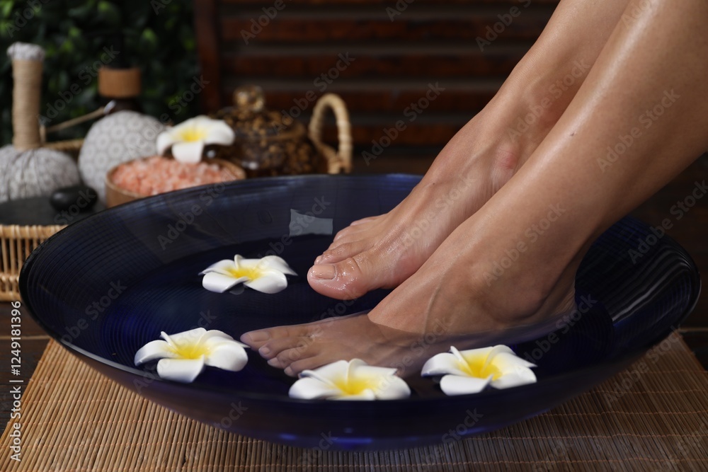 Woman soaking her feet in bowl with water and plumeria flowers on floor, closeup. Spa treatment Woman soaking her feet in bowl with water and plumeria flowers on floor, closeup. Spa treatment