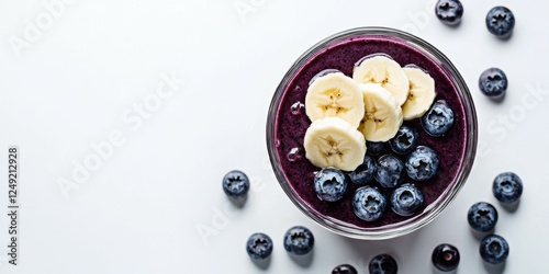 A playful glass of blueberry and banana smoothie topped with sliced bananas, set on a white background
