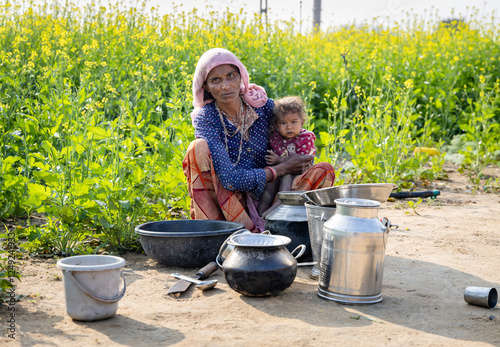 poor malnutrition village women living below poverty line holding baby with mustard fields behind