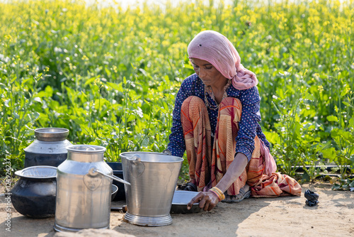 poor malnutrition village women living below poverty line washing dishes with mustard fields behind