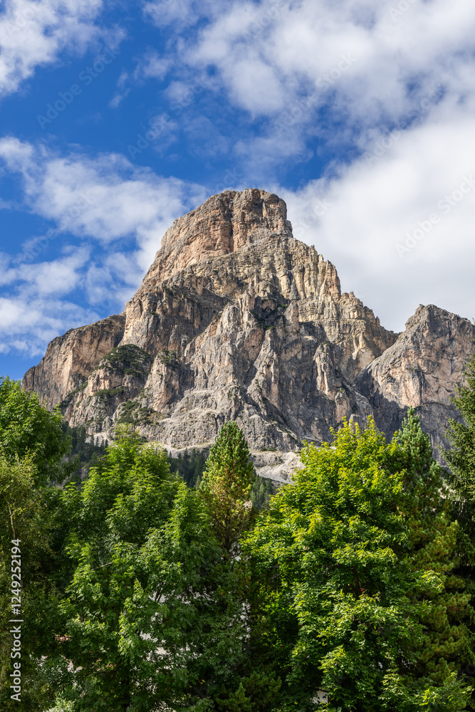 Vertical view of the rugged Sassongher mountain surrounded by dense greenery, with sunlight highlighting its rocky cliffs and alpine beauty Vertical view of the rugged Sassongher mountain surrounded by dense greenery, with sunlight highlighting its rocky cliffs and alpine beauty