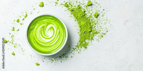 A vibrant matcha latte in a bowl with a swirling design, surrounded by green matcha powder on a white surface.