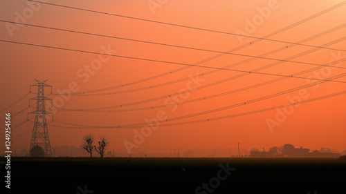 Tall metal power lines stretch across a rural landscape during dawn.