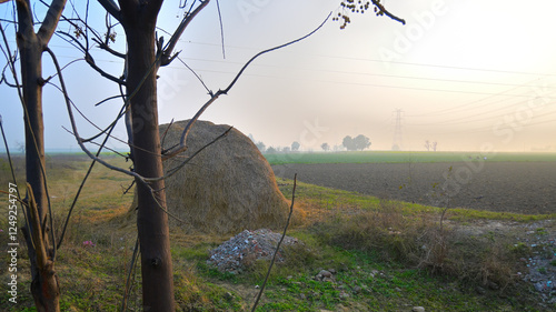 Haystack in a rural landscape, surrounded by open fields and sparse vegetation.