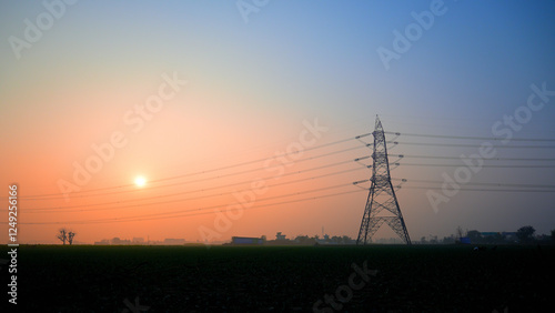 Tall metal power lines stretch across a rural landscape during dawn.