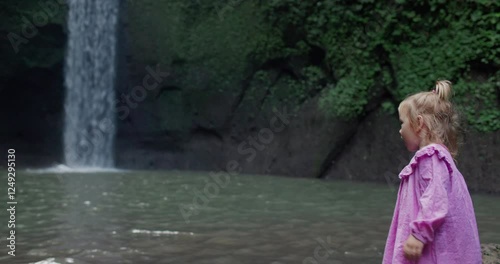 Beautiful little child girl and scenic nature with waterfall in Bali. photo