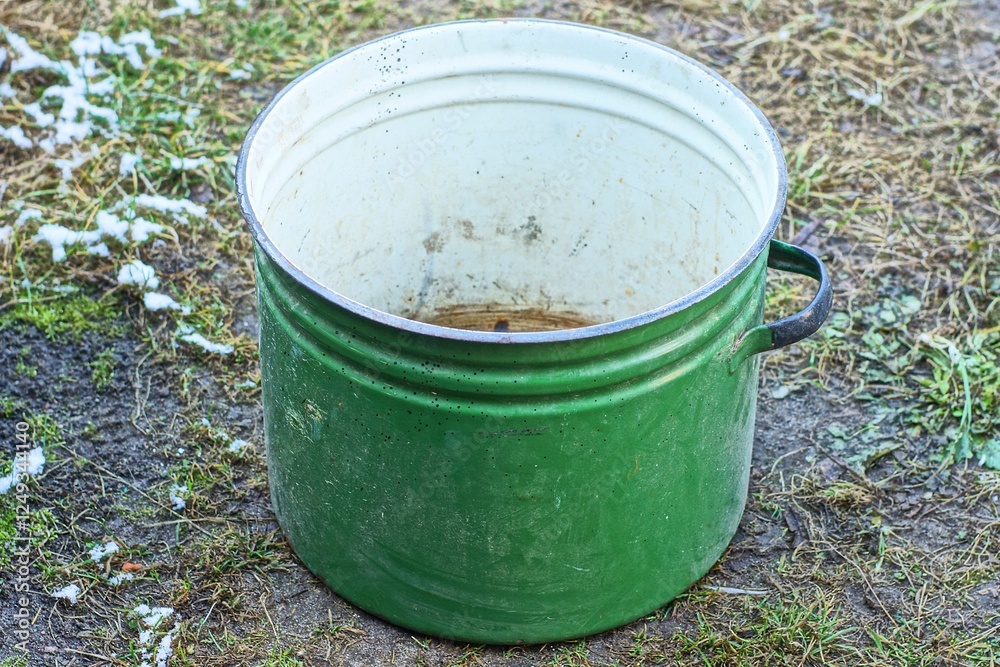 one large enameled kitchen capacious rusty with black handle shiny dirty green open empty old retro round saucepan stands on the ground during the day outdoors one large enameled kitchen capacious rusty with black handle shiny dirty green open empty old retro round saucepan stands on the ground during the day outdoors