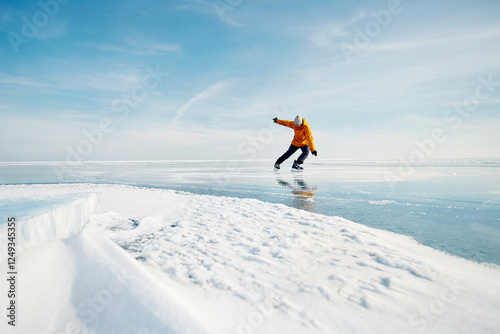 Man in yellow jacket ice skating on frozen lake