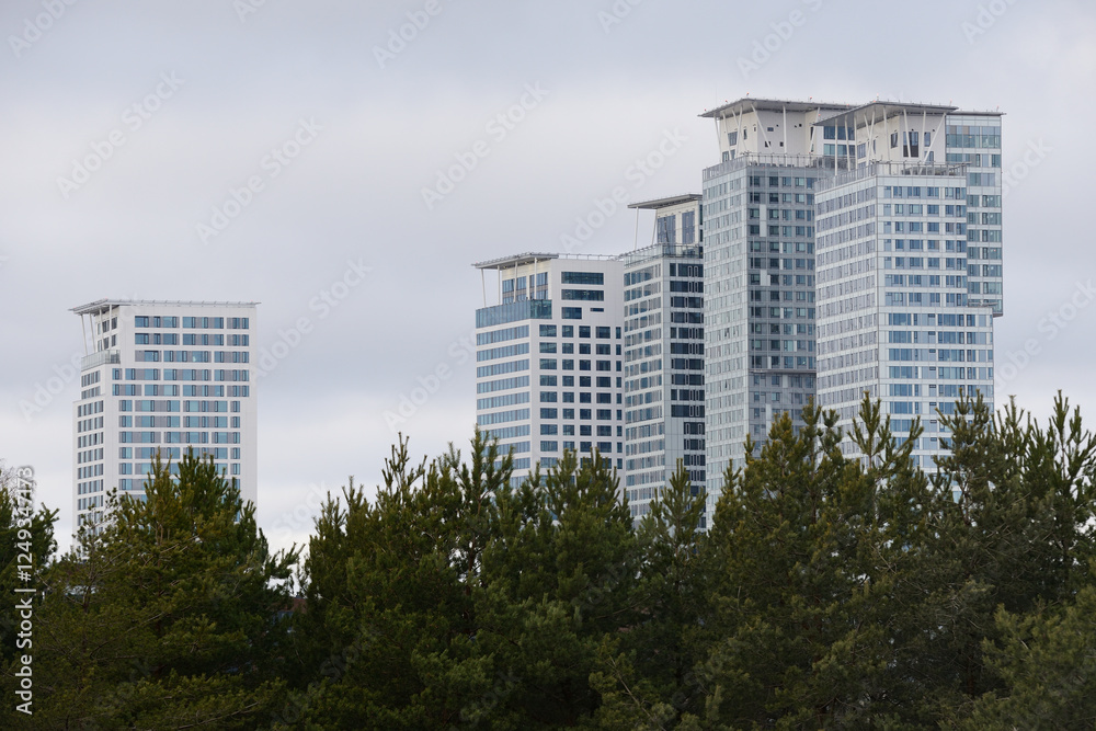 A striking cityscape featuring modern high-rise buildings with sleek glass facades emerging above a dense green foreground of evergreen trees A striking cityscape featuring modern high-rise buildings with sleek glass facades emerging above a dense green foreground of evergreen trees