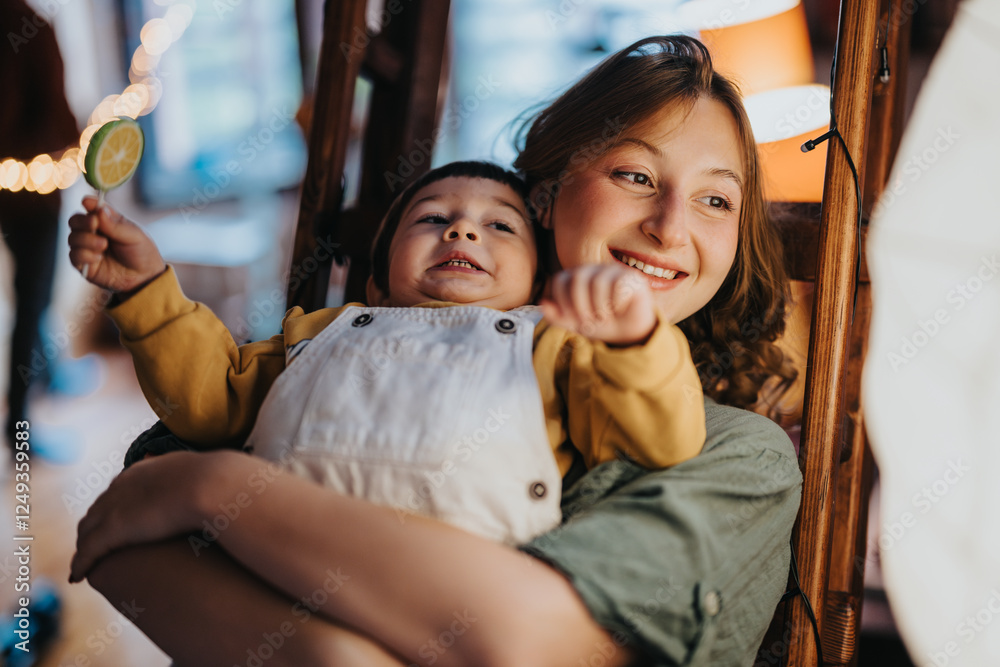 Obraz premium Smiling woman holding a young child, they both appear cheerful. The bright and lively indoor atmosphere conveys happiness and warmth, capturing a moment of family connection.