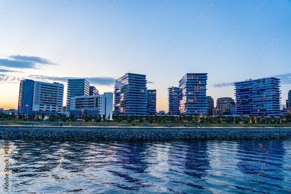 Fototapeta premium Vue panoramique des buildings modernes du quartier de Zeytinburnu à Istanbul, photographiés depuis un bateau sur la mer de Marmara. Le coucher du soleil illumine les façades vitrées des immeubles, tan
