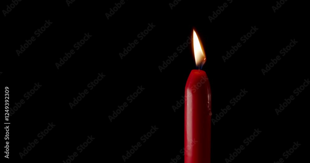A single red candle burning. Isolated candle burning with dark background. Red paraffin candle with yellow shades burns on a black background. Background or illustration of remembrance or celebration. A single red candle burning. Isolated candle burning with dark background. Red paraffin candle with yellow shades burns on a black background. Background or illustration of remembrance or celebration.