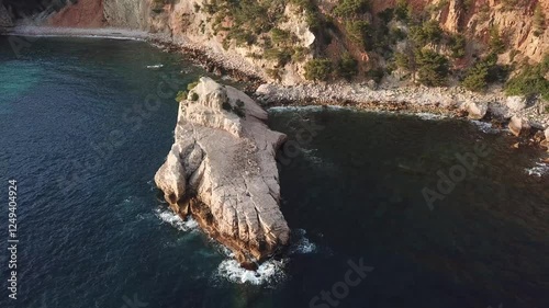 A rocky coastal area of Bandol, France.  The shoreline is rocky with sparse vegetation, including shrubs and trees, with a backdroop of cliff and greenery.