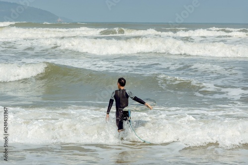 Young asian male surfer entering ocean waves with surfboard