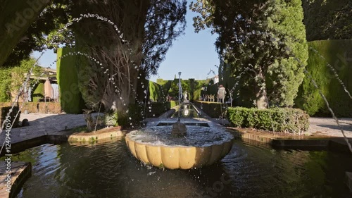 Slow motion gimbal shot of fountain surrounded by trees in Gardens of the Generalife in Alhambra. Granada, Spain. Serene beauty ofGeneralife gardens in Alhambra with stunning fountains 