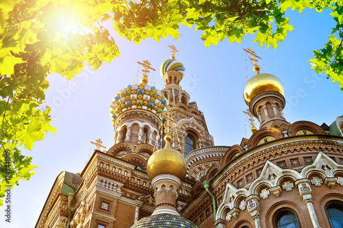 Cathedral of Our Savior on Spilled Blood in Saint-Petersburg, Russia - closeup of architectural landmark framed by green leaves with bright sunlight photo