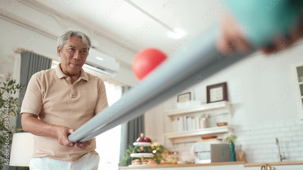 Elderly man playing a ball rolling game with his partner at home, practicing hand-eye coordination, focus, and motor skills for mental and physical wellness. Preventing healthcare concept. Myrmidon. Elderly man playing a ball rolling game with his partner at home, practicing hand-eye coordination, focus, and motor skills for mental and physical wellness. Preventing healthcare concept. Myrmidon.