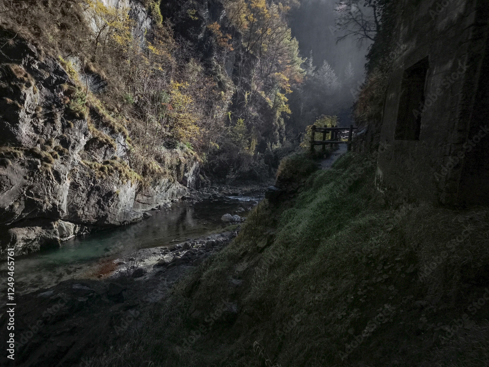 Tranquil mountain stream meanders through rocky gorge in aosta, italy, surrounded by autumn foliage and misty atmosphere under soft sunlight Isollaz waterfall