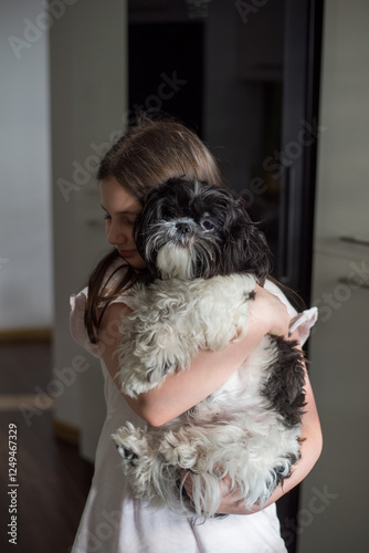 A girl in a white outfit hugging her small black and white dog on a cozy bed.