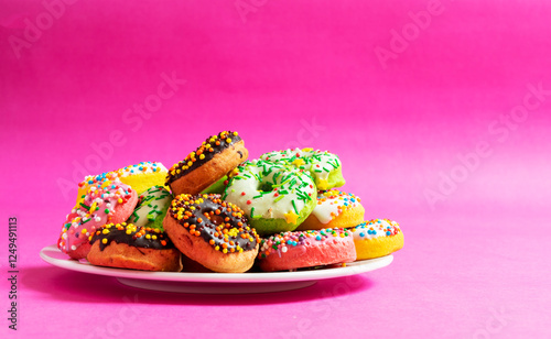 Colorful donuts on a white plate on red, pink background.