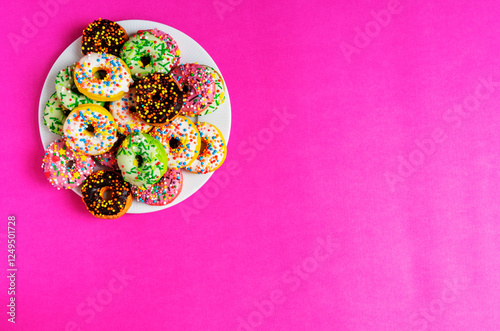 Colorful donuts on a white plate on red, pink background.