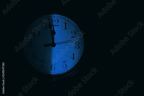The clock face is divided in half by shadow on a dark background. Moonlight.