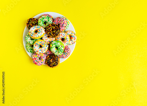 Colorful donuts on a white plate on yellow background