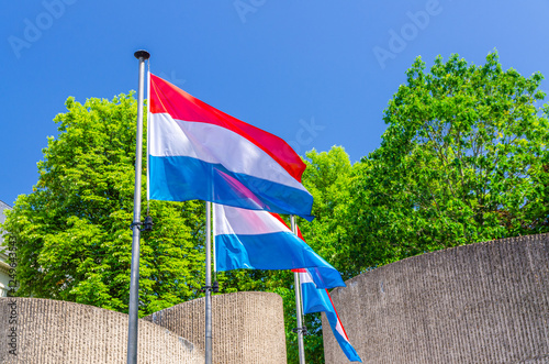 Luxembourg flags in front of National Monument of Solidarity at Cannon Hill Kanounenhiwwel, green trees and blue sky in Luxembourg city historical centre