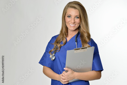 Attractive young Caucasian female medical professional - in blue scrubs wearing a stethoscope and holding a clipboard