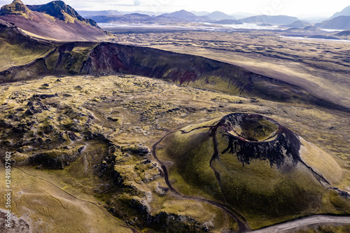 Stunning aerial image showcasing a volcanic crater surrounded Landmannalaugar mountains and by hills and expansive wilderness, emphasizing the raw beauty and geology of volcanic regions in Iceland