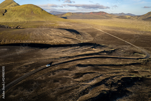 Aerial perspective of a car navigating a sparse basalt road Landmannalaugar in Iceland, surrounded by barren landscapes and bathed in warm sunlight