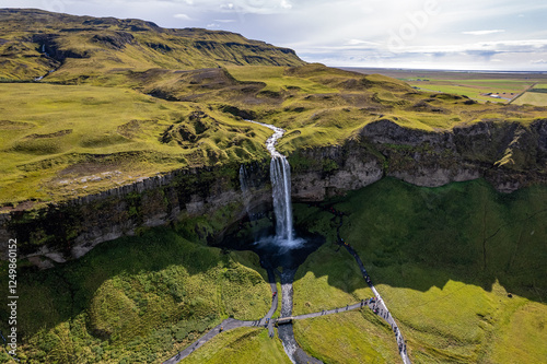 A magnificent aerial view Seljalandsfoss waterfall in Iceland plunges over the edge of green cliffs, surrounded by stunning countryside. The serene landscape captures beauty of untouched nature