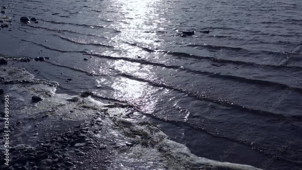 Video-Silvery Reflective Ripples of Water Breaking at the Cold, Frigid, Snowy, Icy Shoreline as the sunsets with Black Rocks-Video Background, backdrop, border Video-Silvery Reflective Ripples of Water Breaking at the Cold, Frigid, Snowy, Icy Shoreline as the sunsets with Black Rocks-Video Background, backdrop, border
