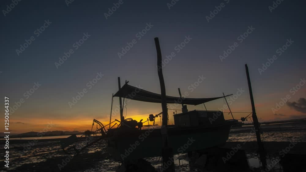 Fishing boat silhouetted against a beautiful sunrise after low tide in a serene coastal setting Fishing boat silhouetted against a beautiful sunrise after low tide in a serene coastal setting