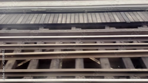 A train moves swiftly over well-maintained railway tracks. The surroundings display urban infrastructure under a clear sky, showcasing a busy city vibe
