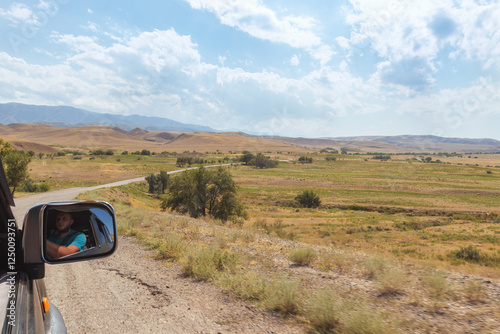Rural Gravel Road Through Rolling Hills Landscape with Car Side View, Winding Country Path in Wilderness