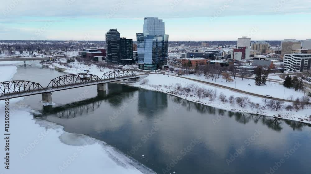 City with a river running through it and a bridge over it. The bridge is in the foreground and the river is in the background. The city is covered in snow and the sky is cloudy