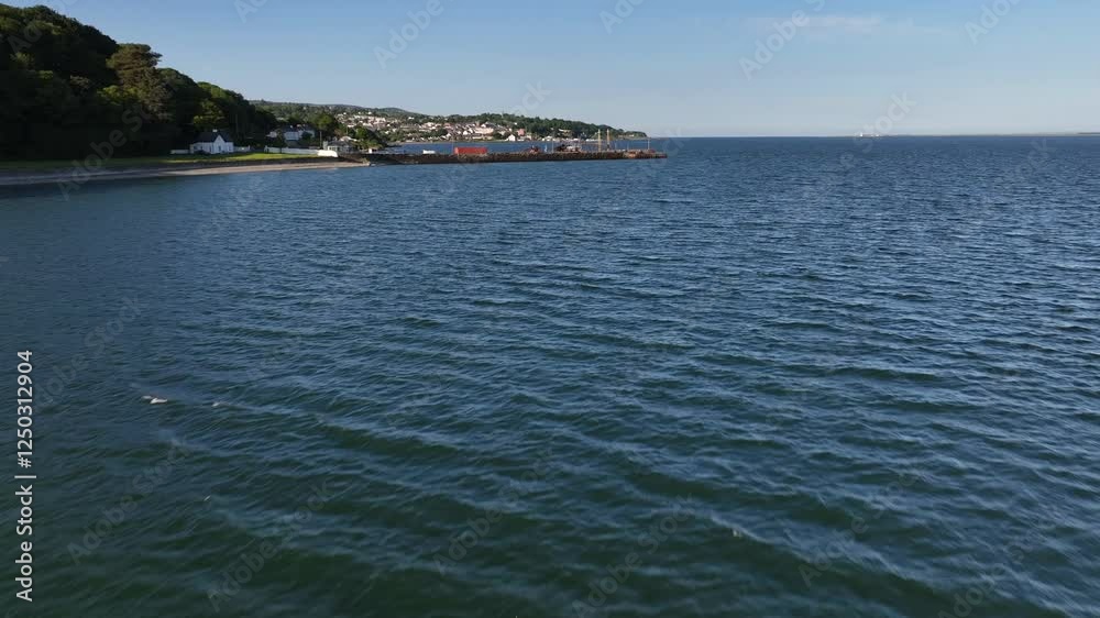 Lough Foyle, County Donegal, Ireland, June 2023. Drone pushes forwards over the water tilting up from the rippling surface showcasing Carrickarory Pier with docked Fishing boats on the quayside.