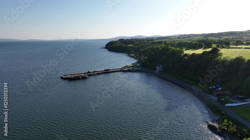 Lough Foyle, County Donegal, Ireland, June 2023. Drone pushes forwards southwest along the waterfront towards Carrickarory Pier, with Redcastle and Quigley’s Point in the background on a sunny day. photo