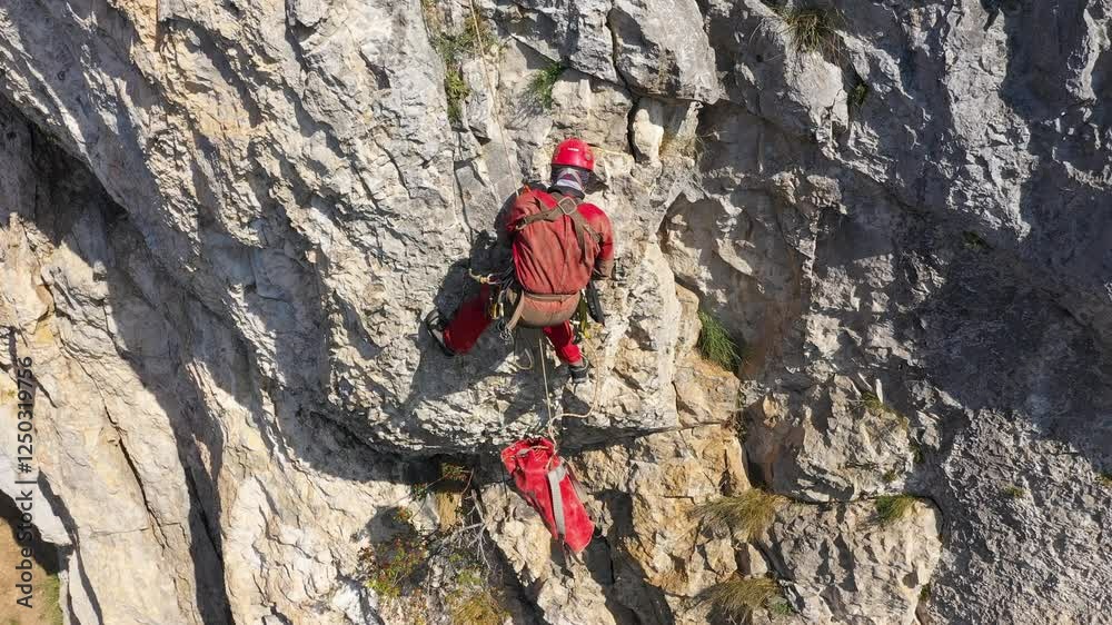 Aerial view of mountain rescuer abseiling on a rocky wall hanging on a rope Aerial view of mountain rescuer abseiling on a rocky wall hanging on a rope