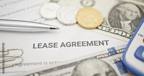 Property rental, leasing contracts, real estate, housing agreements, and property management. A close-up view of a lease agreement document with paperclips, coins, US dollar, and a pen placed on top.