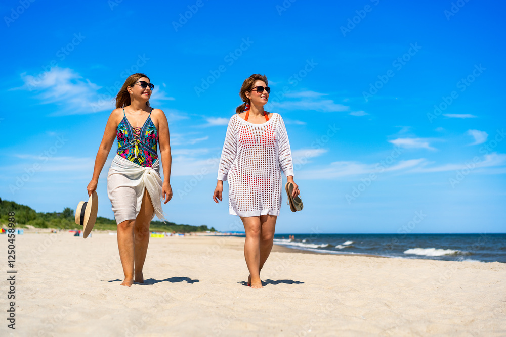 Two beautiful middle aged females walking on white sandy beach in summertime. Front view Two beautiful middle aged females walking on white sandy beach in summertime. Front view