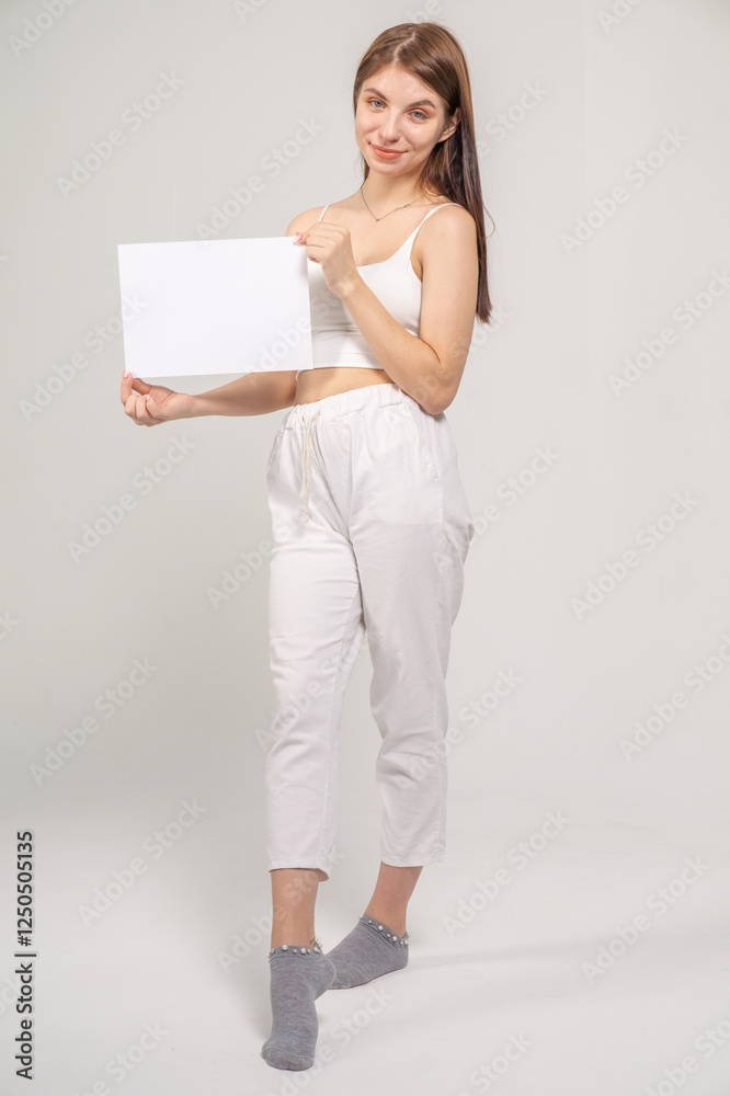 Pretty young brunette standing with a A4 empty paper sheet on a white background. Copyspace Pretty young brunette standing with a A4 empty paper sheet on a white background. Copyspace