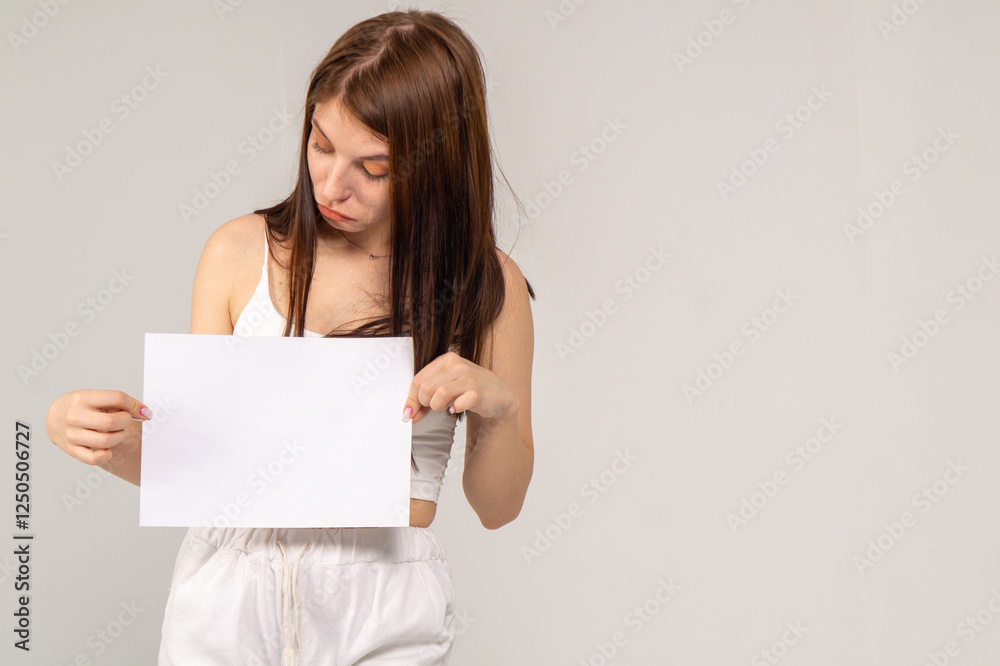 Pretty young brunette standing with a A4 empty paper sheet on a white background. Copyspace Pretty young brunette standing with a A4 empty paper sheet on a white background. Copyspace