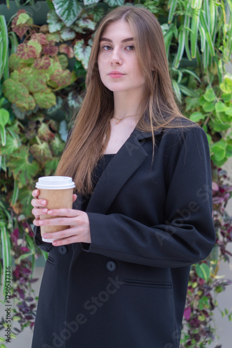 Pretty young girl with a cup of coffee against the background of a green hedge photo