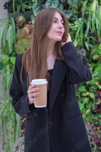 Pretty young girl with a cup of coffee against the background of a green hedge photo