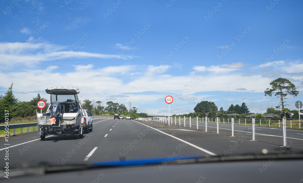 Car towing a boat on Waikato Expressway. 110 kmh road speed signs by the side of highway. New Zealand.